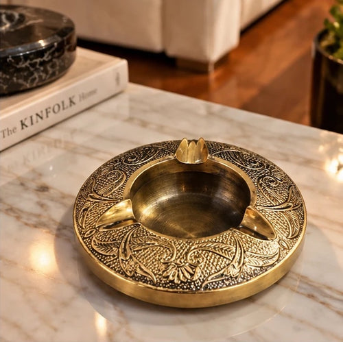 Embossed brass ashtray styled on a marble coffee table beside books