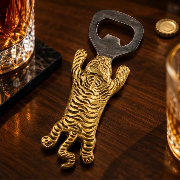 Brass tiger bottle opener on a dark wooden bar beside a crystal whisky glass