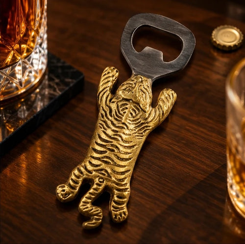 Brass tiger bottle opener on a dark wooden bar beside a crystal whisky glass