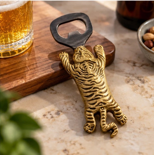 Brass tiger bottle opener on a walnut serving board with a glass of beer