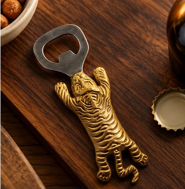 Brass tiger bottle opener on a walnut table next to a bottle cap